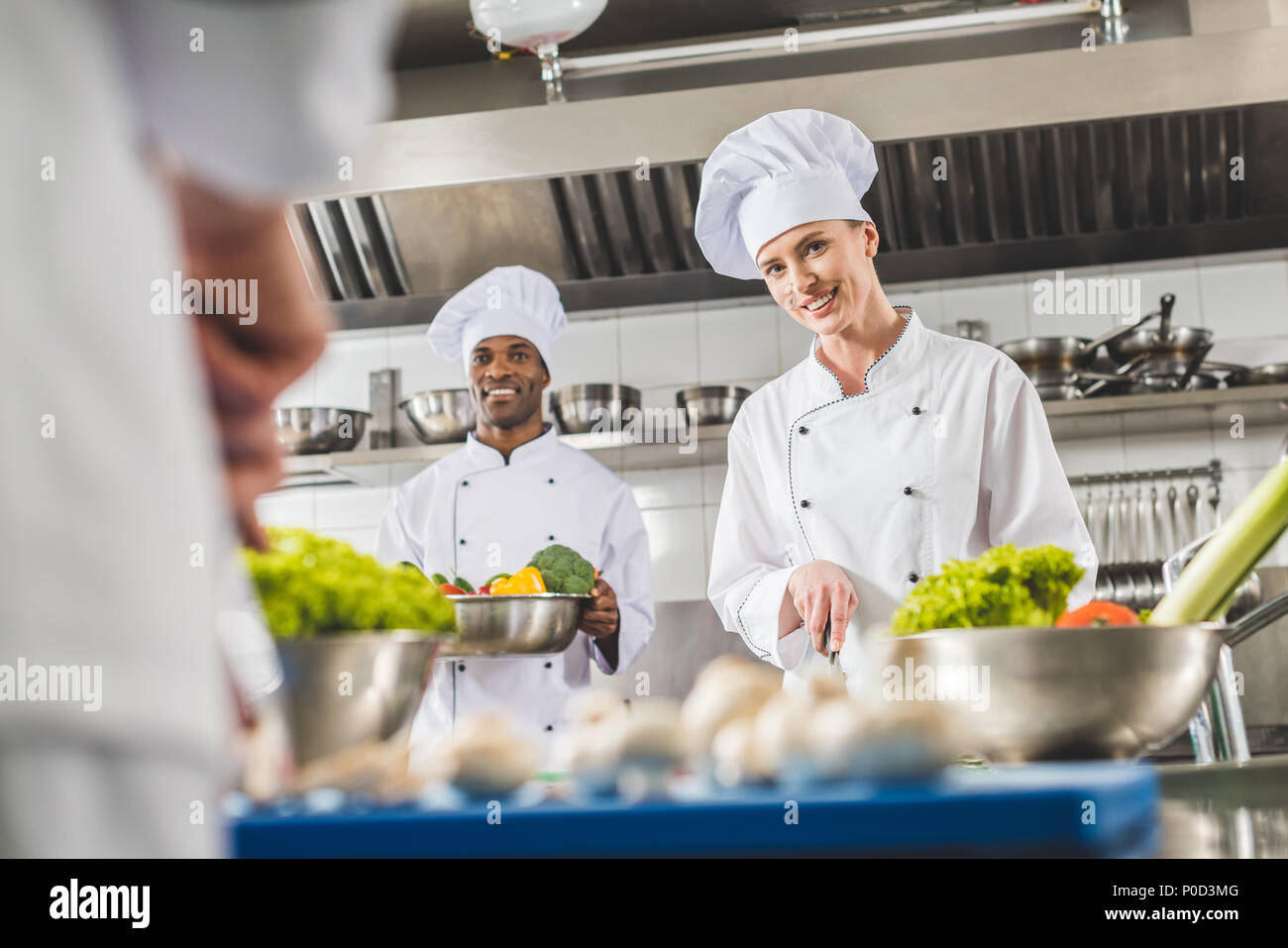 smiling multicultural chefs preparing food at restaurant kitchen and looking at camera Stock Photo