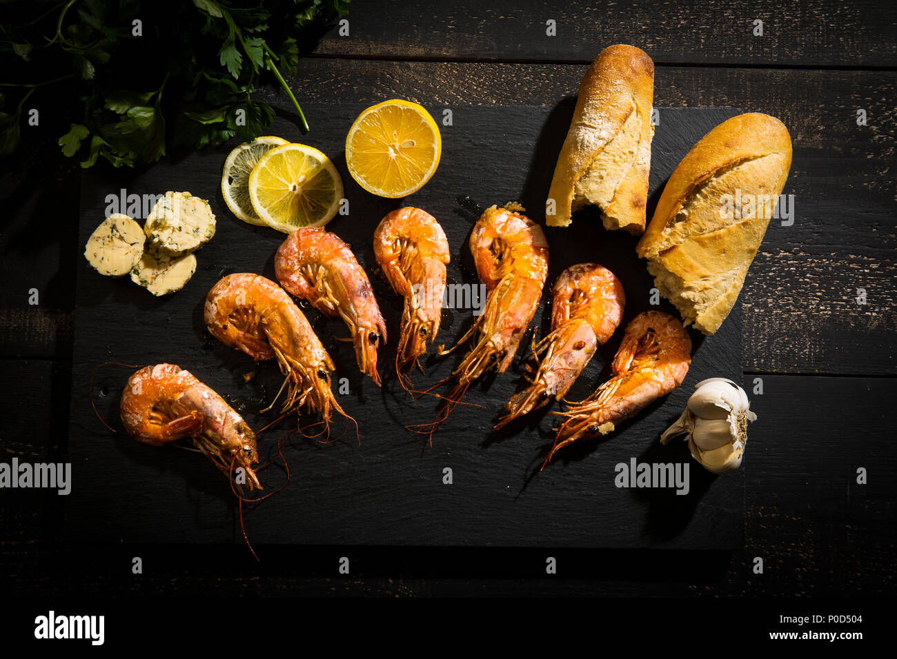 gegrillte Argentinische Rotgarnelen mit Baguette, Kräuterbutter und Zitrone auf dunklem Untergrund Stock Photo