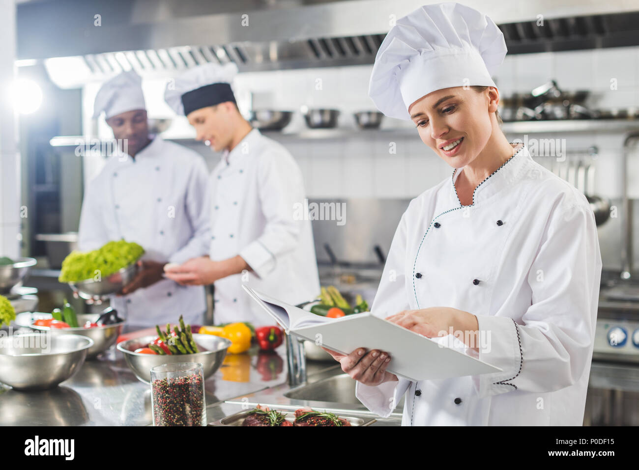 attractive chef reading recipe in recipe book at restaurant kitchen ...
