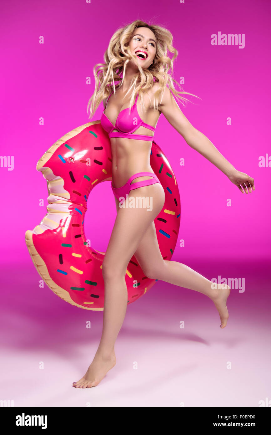 Happy young woman in swimsuit running with swimming tube in shape of doughnut Stock Photo