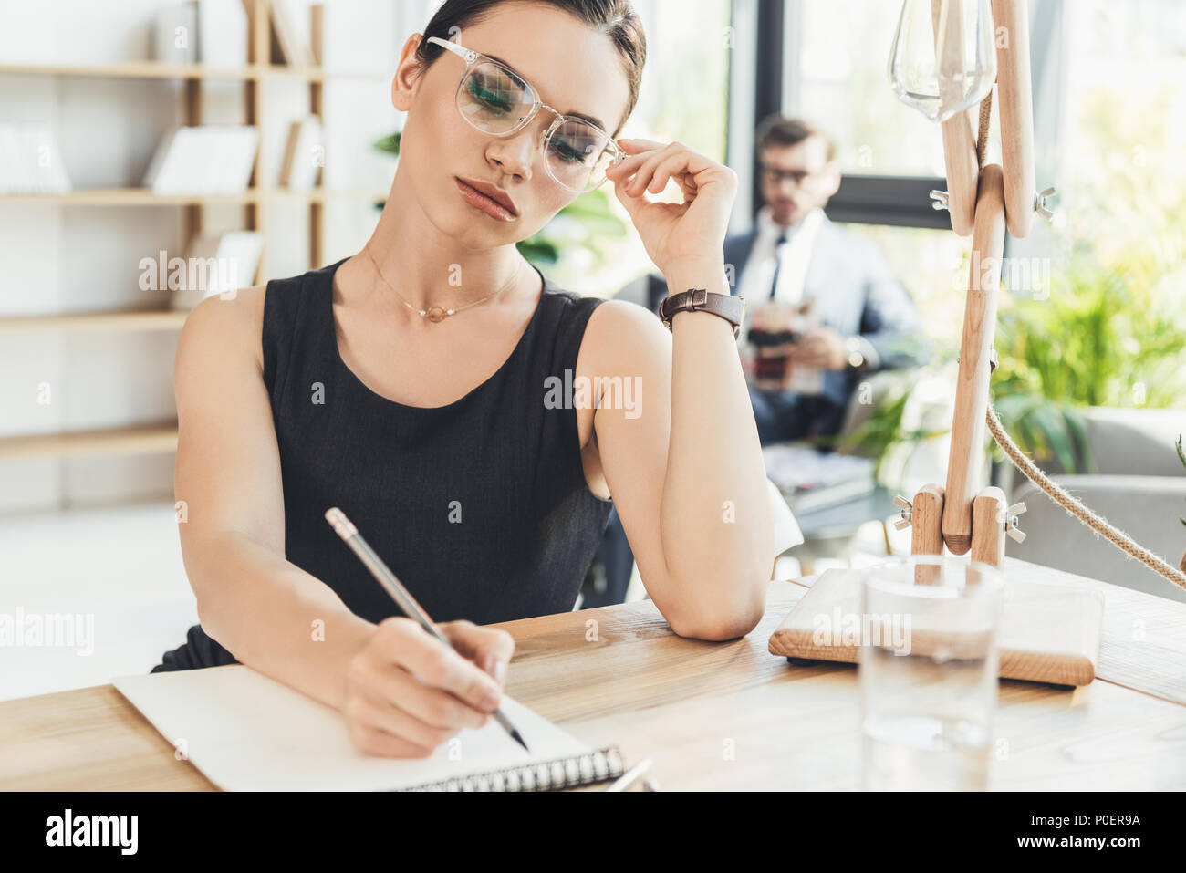 Young beautiful businesswoman sitting in office at desk and writing in ...