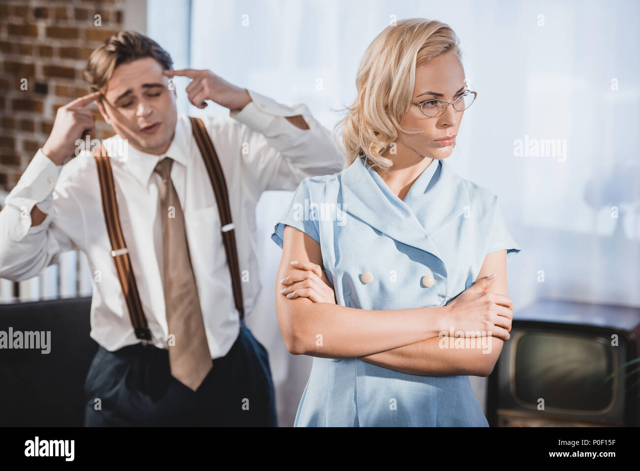 offended woman standing with crossed arms and looking away while emotional husband gesturing with hands behind, 1950s style Stock Photo