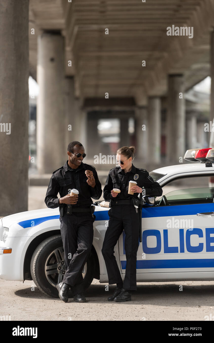 police officers with coffee and doughnuts standing next to car Stock