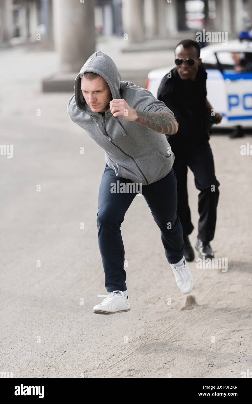 young hooded thief running from african american policeman Stock Photo
