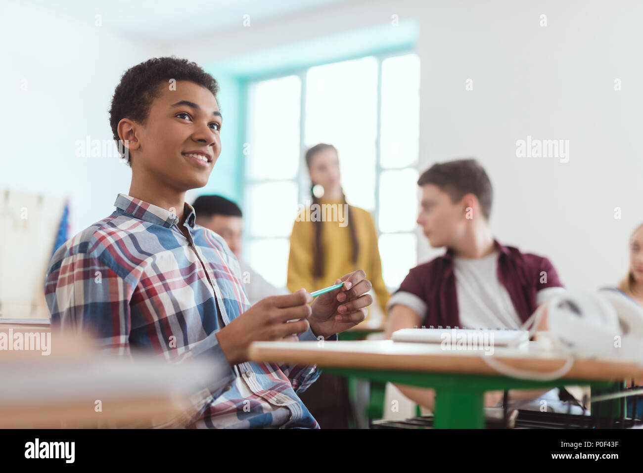 Low angle view of african american high school student holding pencil in hand and classmates sitting behind Stock Photo