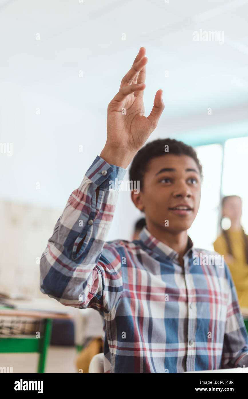 African american teenage student with arm up and classmates behind in