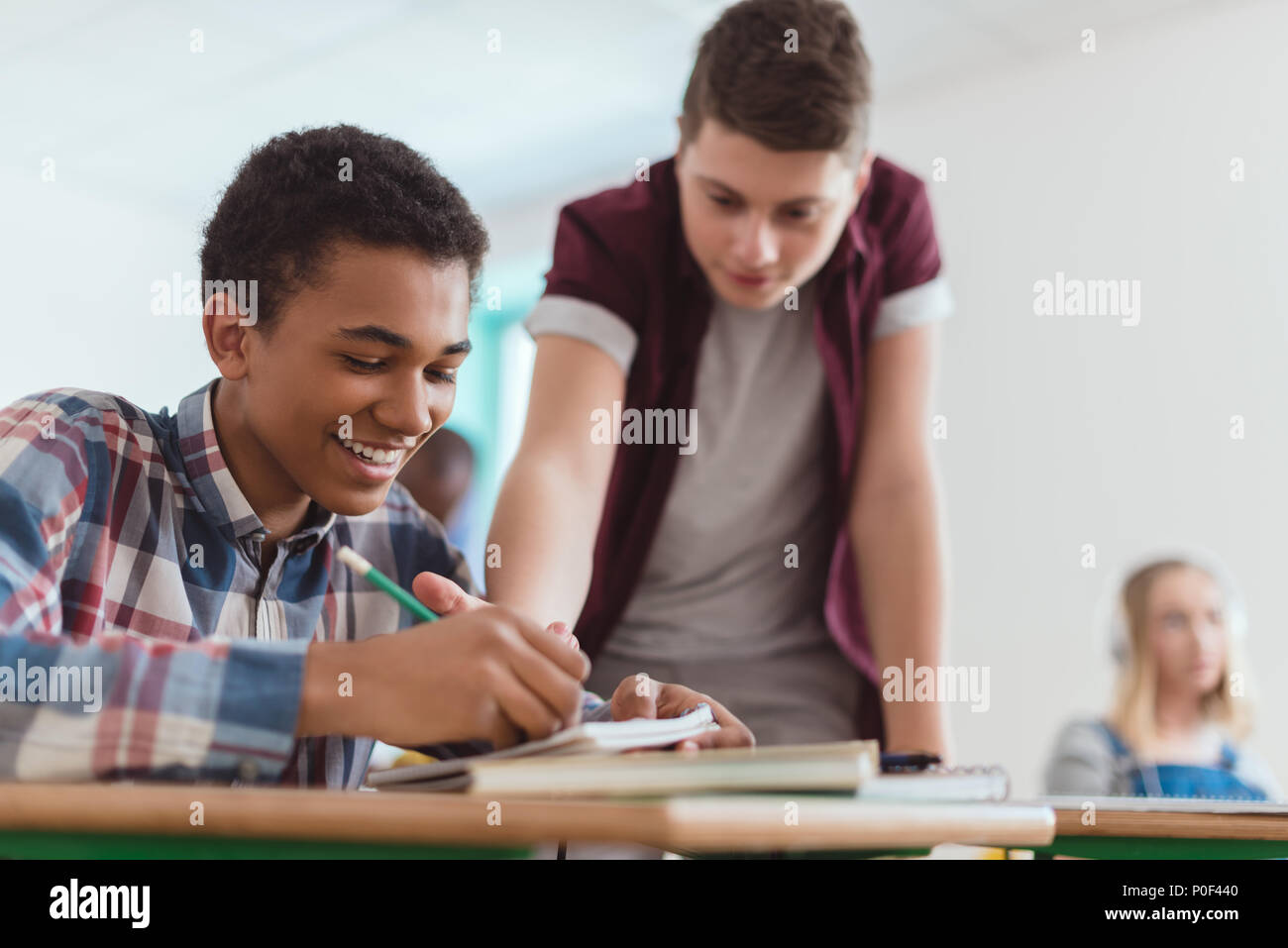Smiling african american boy writing in textbook with classmate standing behind Stock Photo