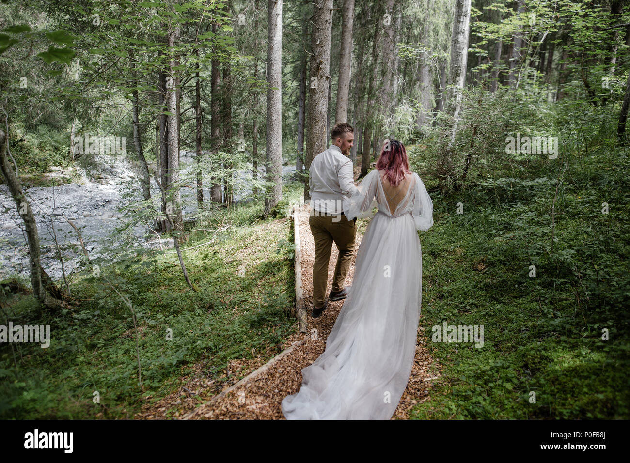 back view of beautiful young wedding couple walking on mountain path in ...