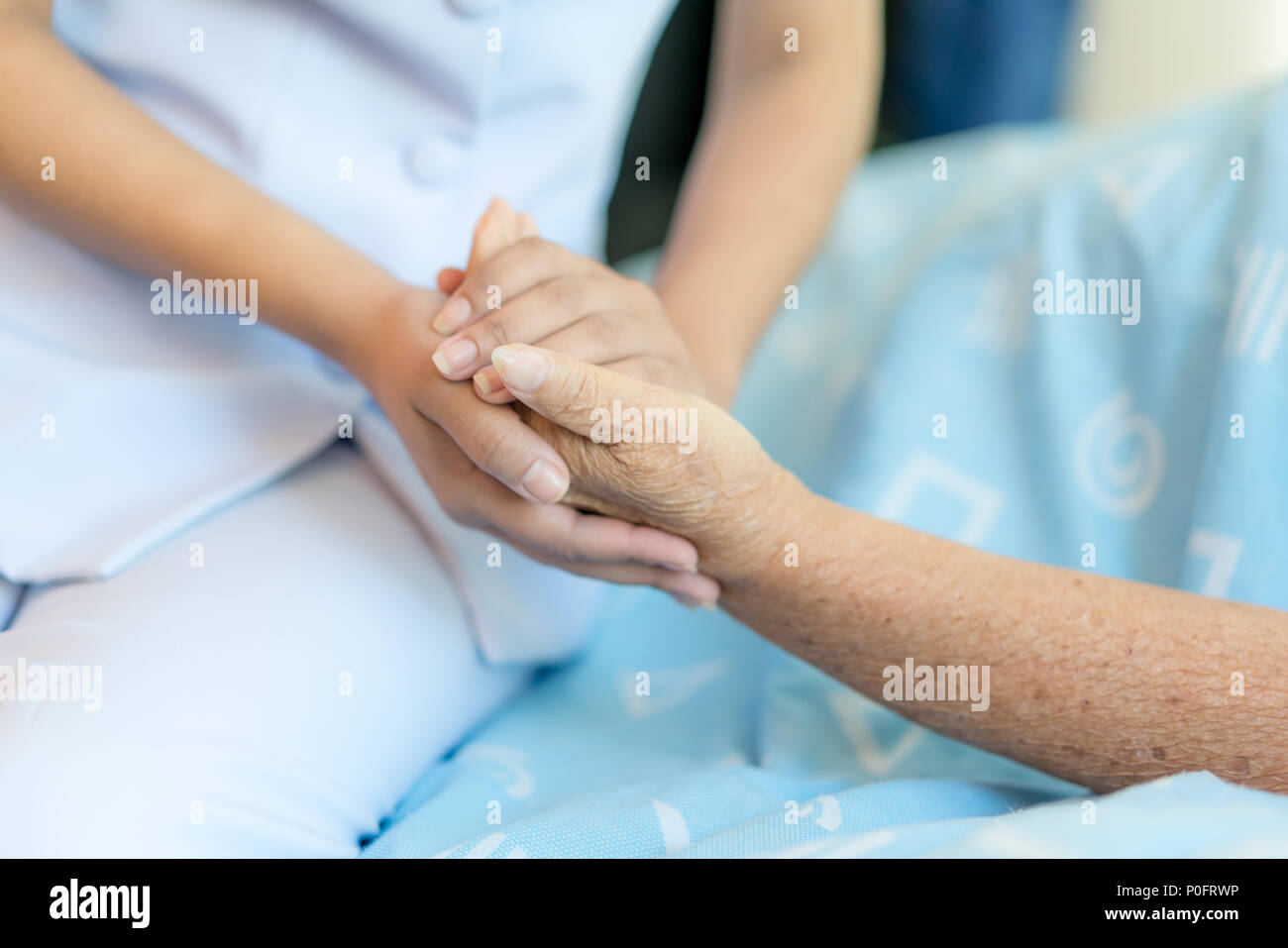 Nurse sitting on a hospital bed next to an older woman helping hands