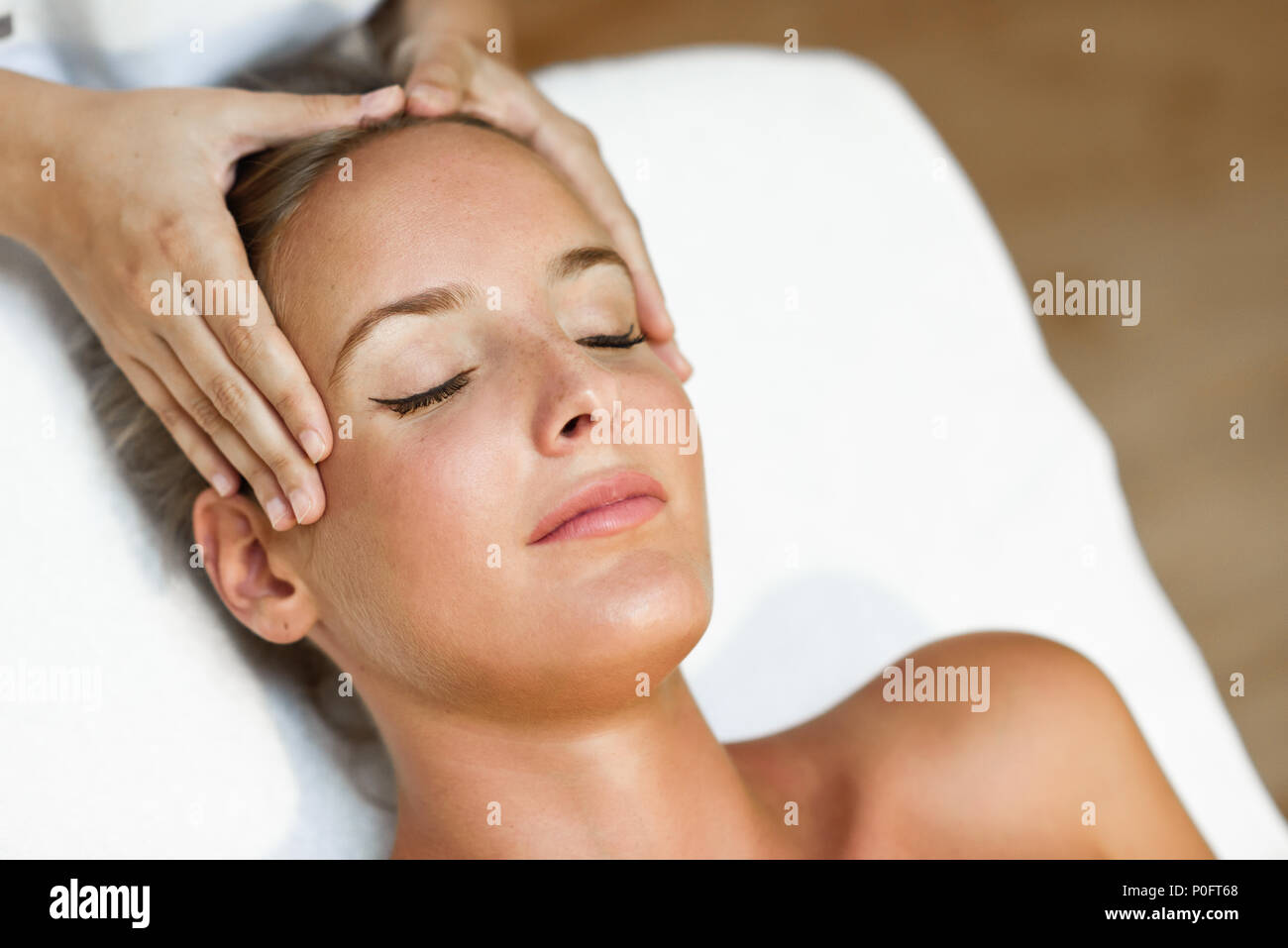Young blond woman receiving a head massage in a spa center with eyes closed. Female patient is receiving treatment by professional therapist. Stock Photo