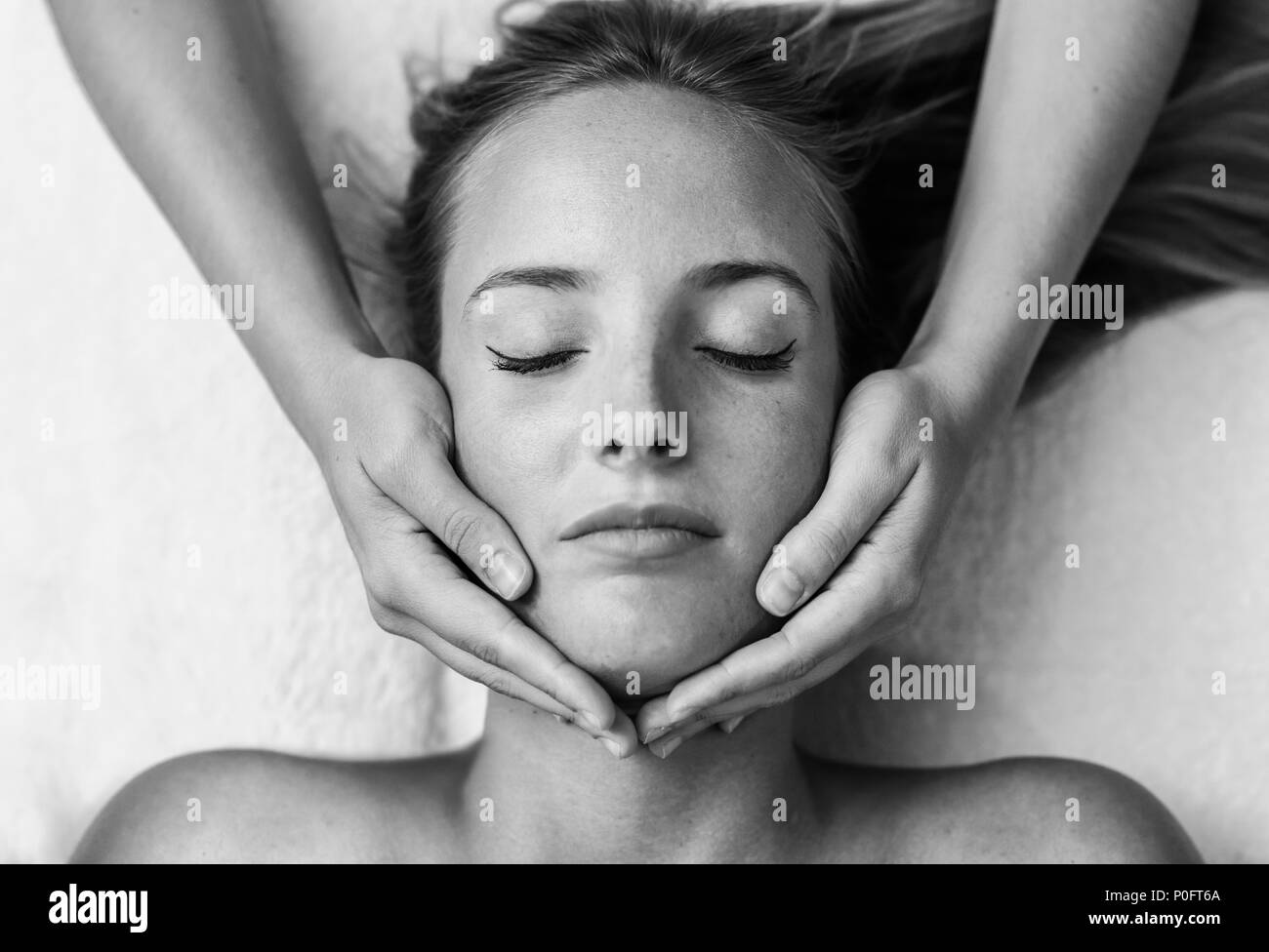 Young blond woman receiving a head massage in a spa center with eyes closed. Female patient is receiving treatment by professional therapist. Stock Photo