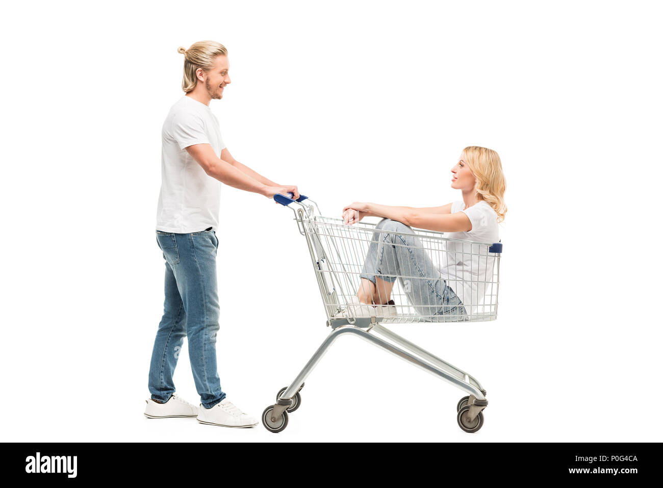 side view of smiling man holding shopping cart with woman sitting in