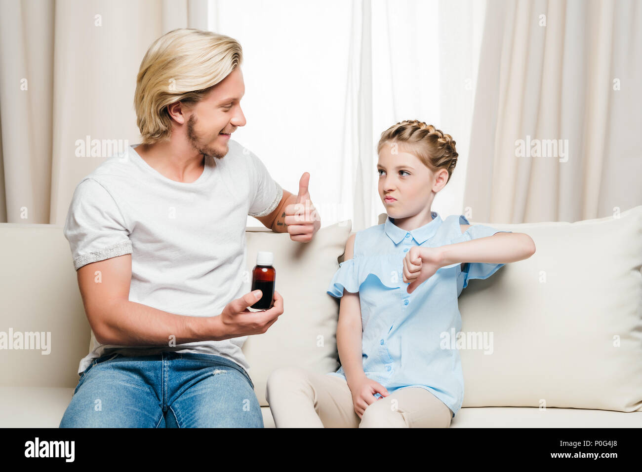 Smiling father holding medicine and showing thumb up while daughter showing thumb down Stock Photo