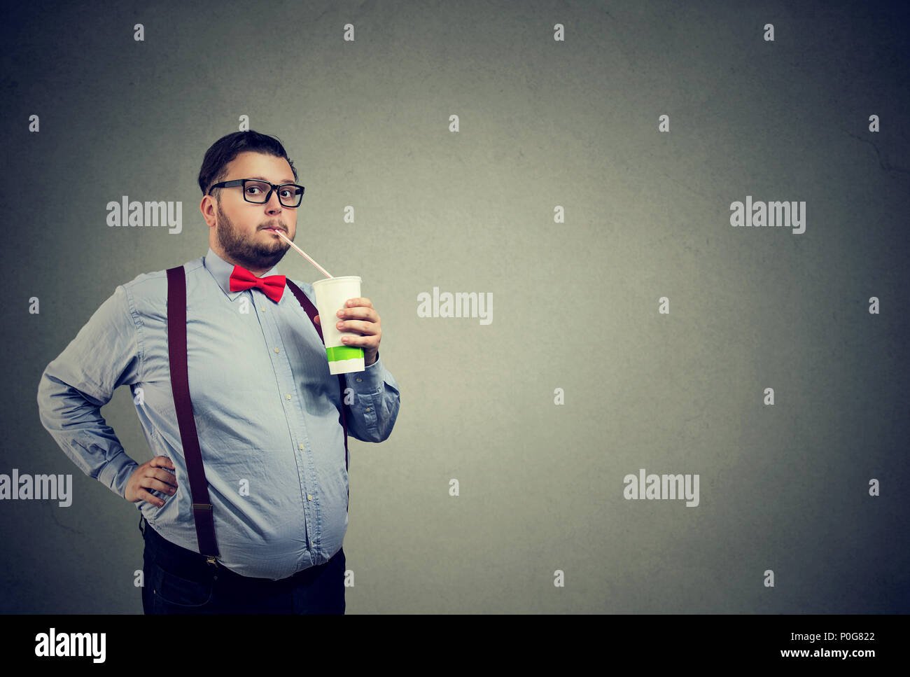 Formal chubby man in bow tie and glasses consuming sweet soda water looking at camera on gray Stock Photo