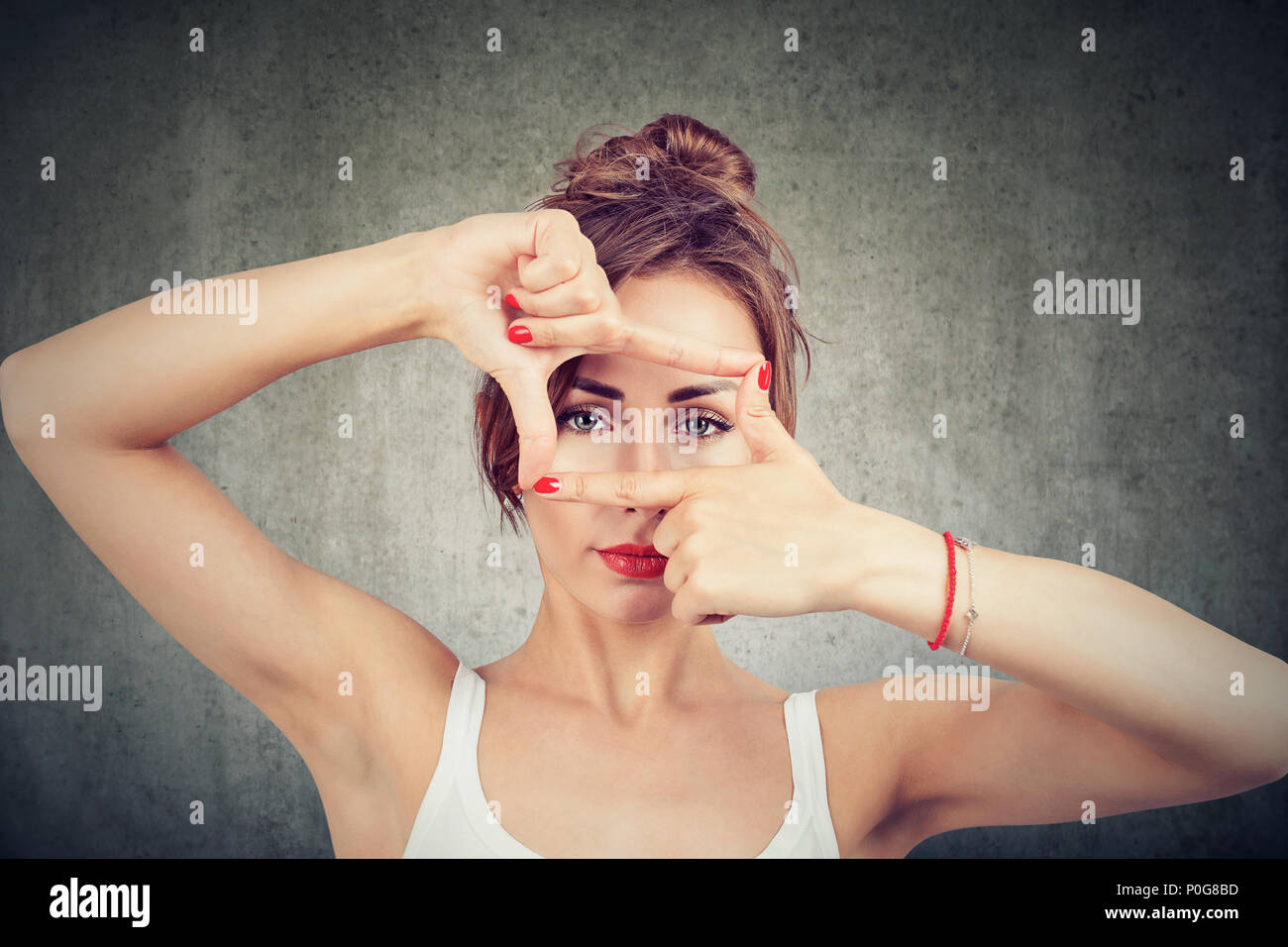 Young girl making frame with fingers and looking through limits at camera on gray background Stock Photo