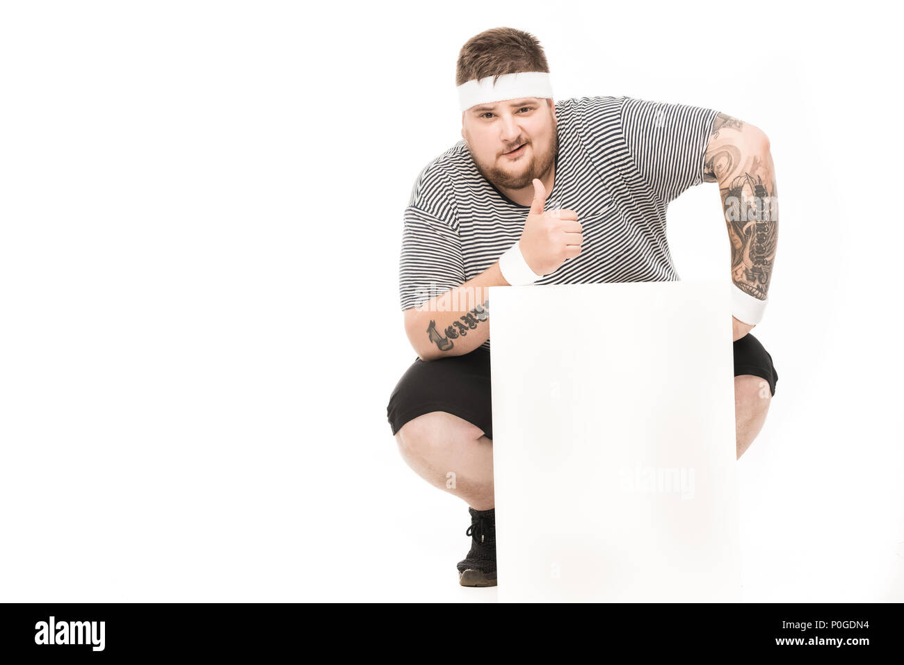 young man showing thumb up while squatting down near empty banner isolated on white Stock Photo