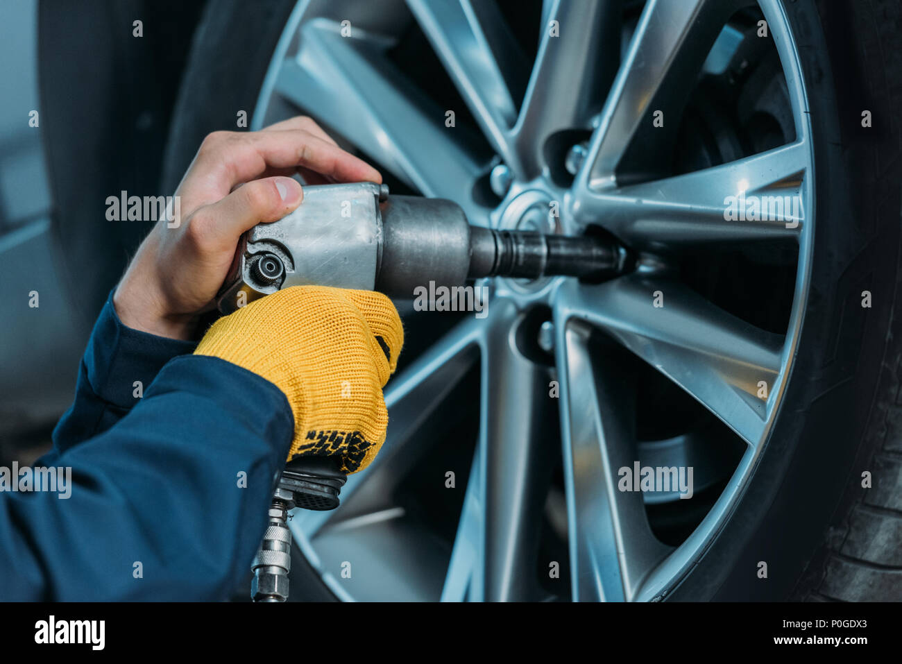 Cropped shot of automechanic unscrewing tire bolts on a lifted up car at a repair shop. Stock Photo