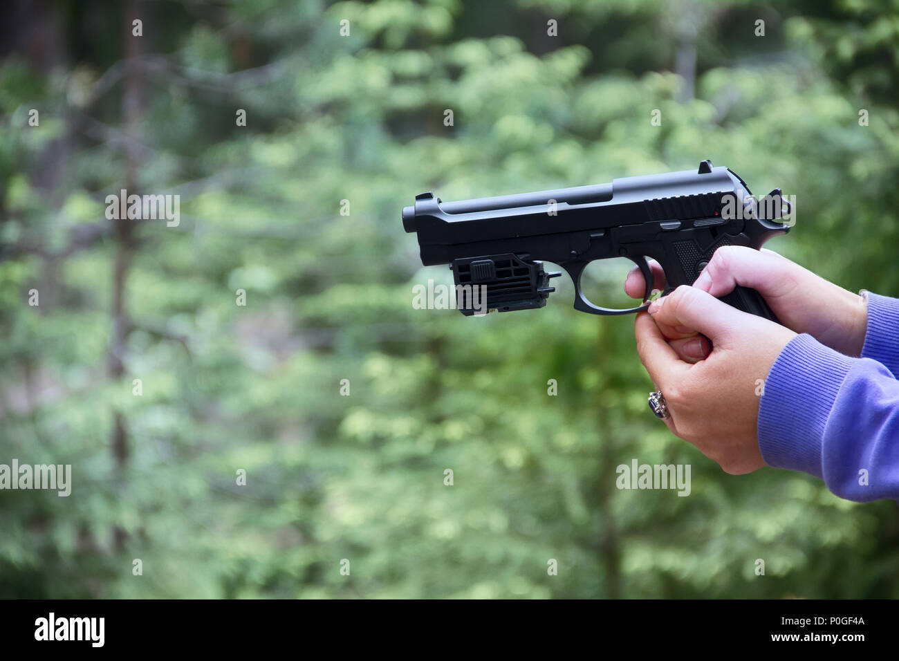 Woman shoots from airgun pistol (black air gun) in forest. Hands and