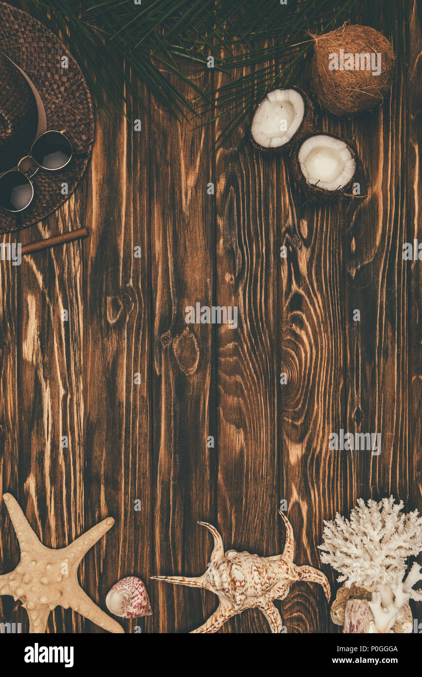 top view of seashells with coconuts and straw hat on wooden surface ...