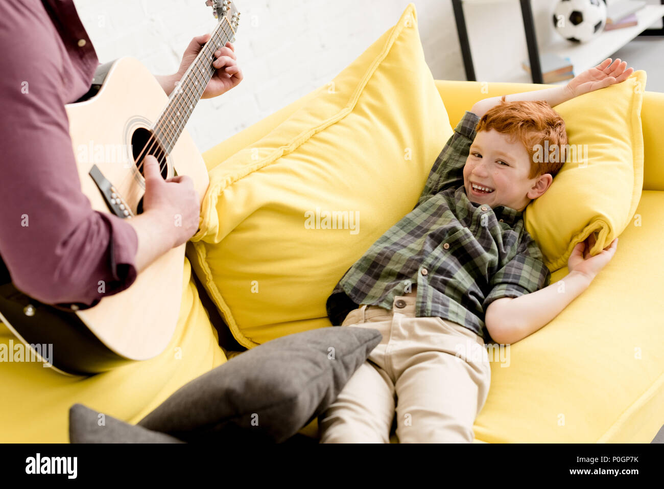 cropped shot of father playing guitar while cute happy son lying on couch Stock Photo