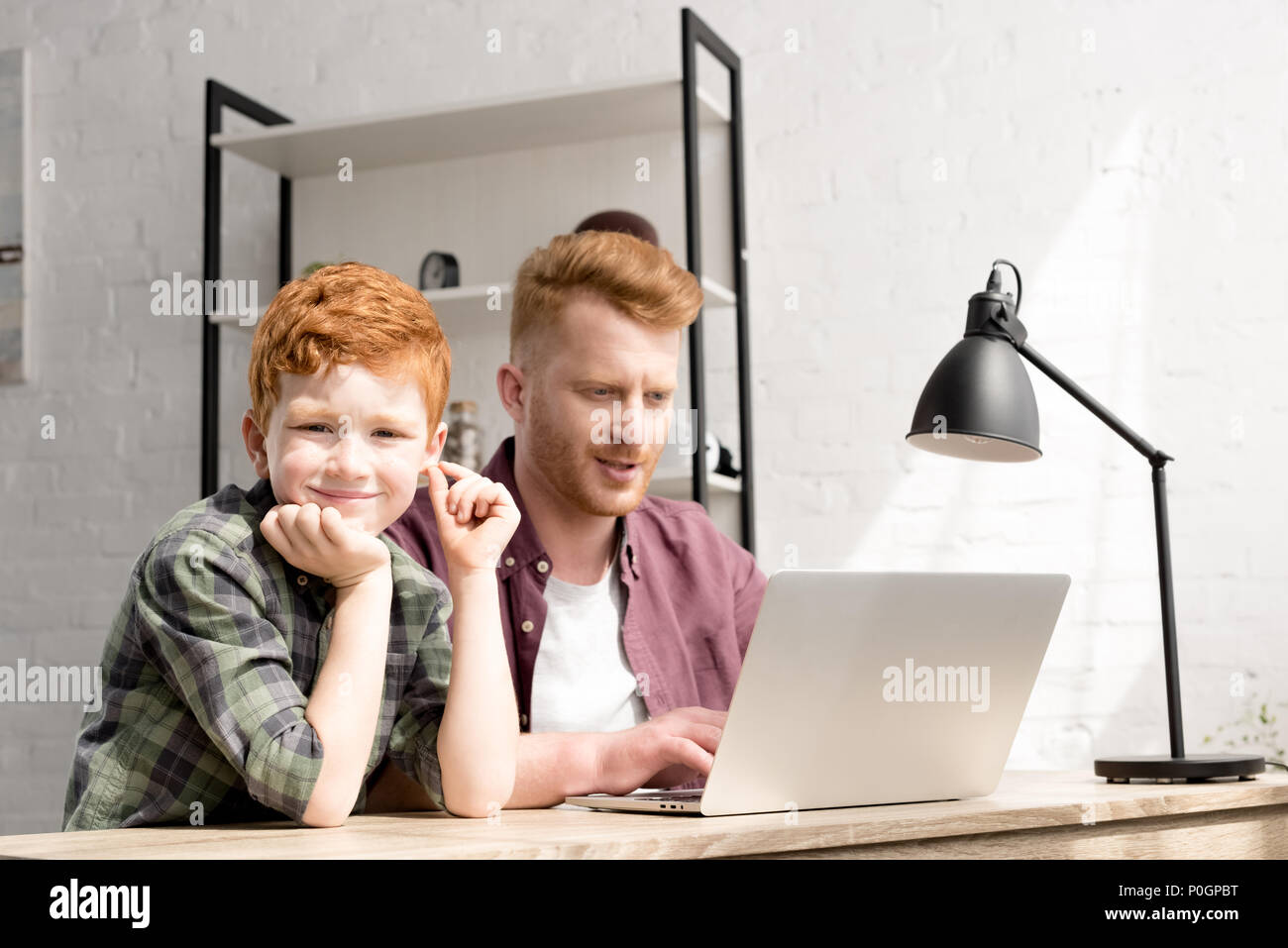 cute little boy smiling at camera while using laptop with father at ...