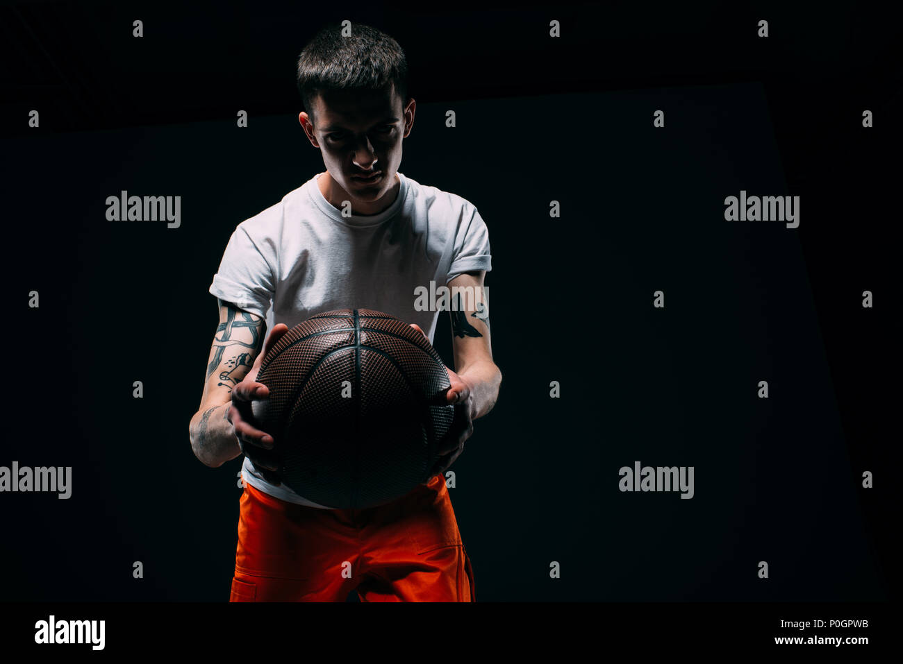 Man in prison uniform holding basketball ball on dark background Stock Photo