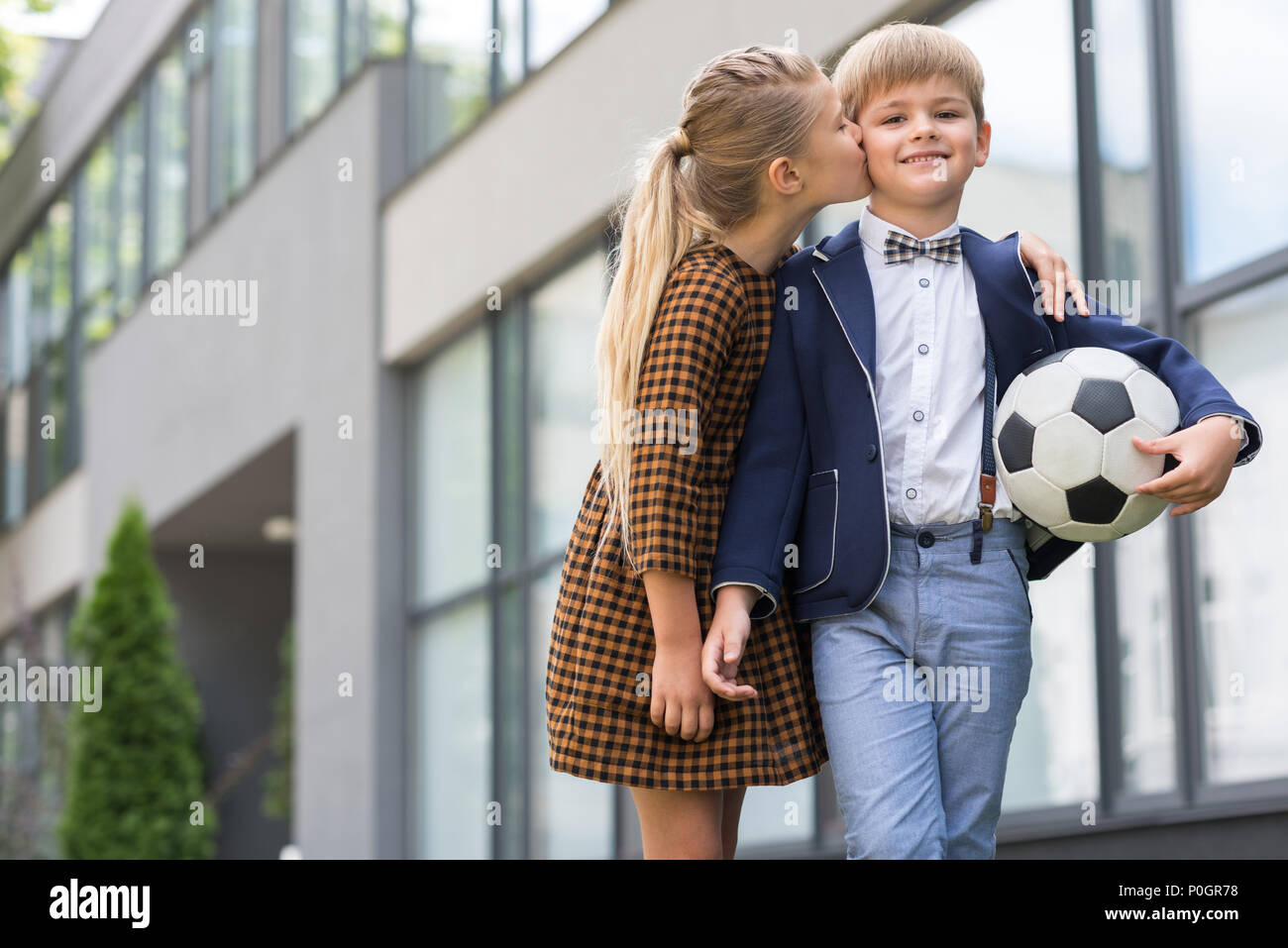 cute schoolgirl in dress kissing happy schoolboy with soccer ball Stock Photo