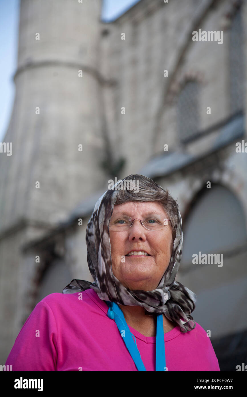 woman outside blue mosque with grey headscarf and pink sweater, mosque in background vertical Stock Photo