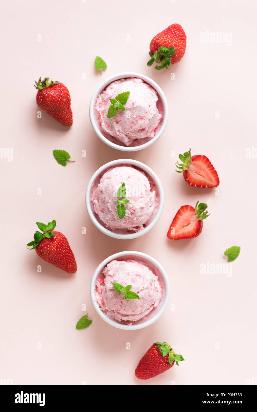 Strawberry ice cream and fresh strawberries flat lay on pink pastel background. Three bowls of