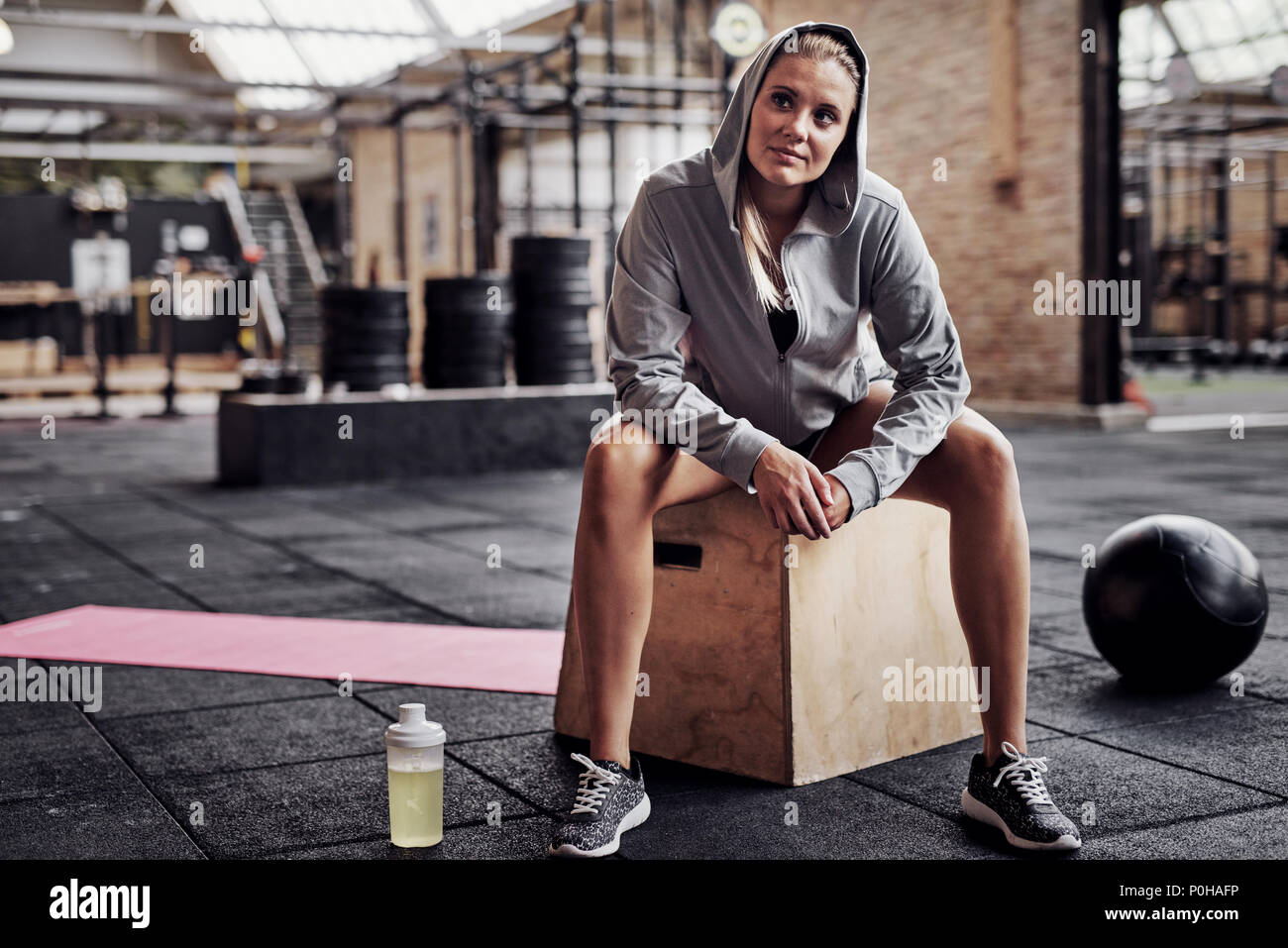 Smiling young blonde woman in exercise clothing sitting alone on a box in a  gym thinking about her workout Stock Photo - Alamy
