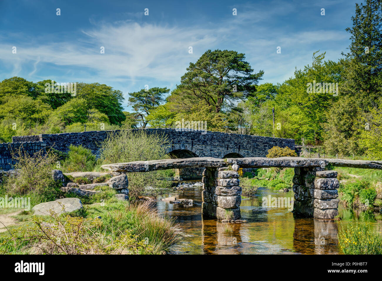 A landscape of the ancient clapper bridge at Postbridge in the Dartmoor National Park, Devon taken in Springtime with blue sky and vibrant greenery. Stock Photo