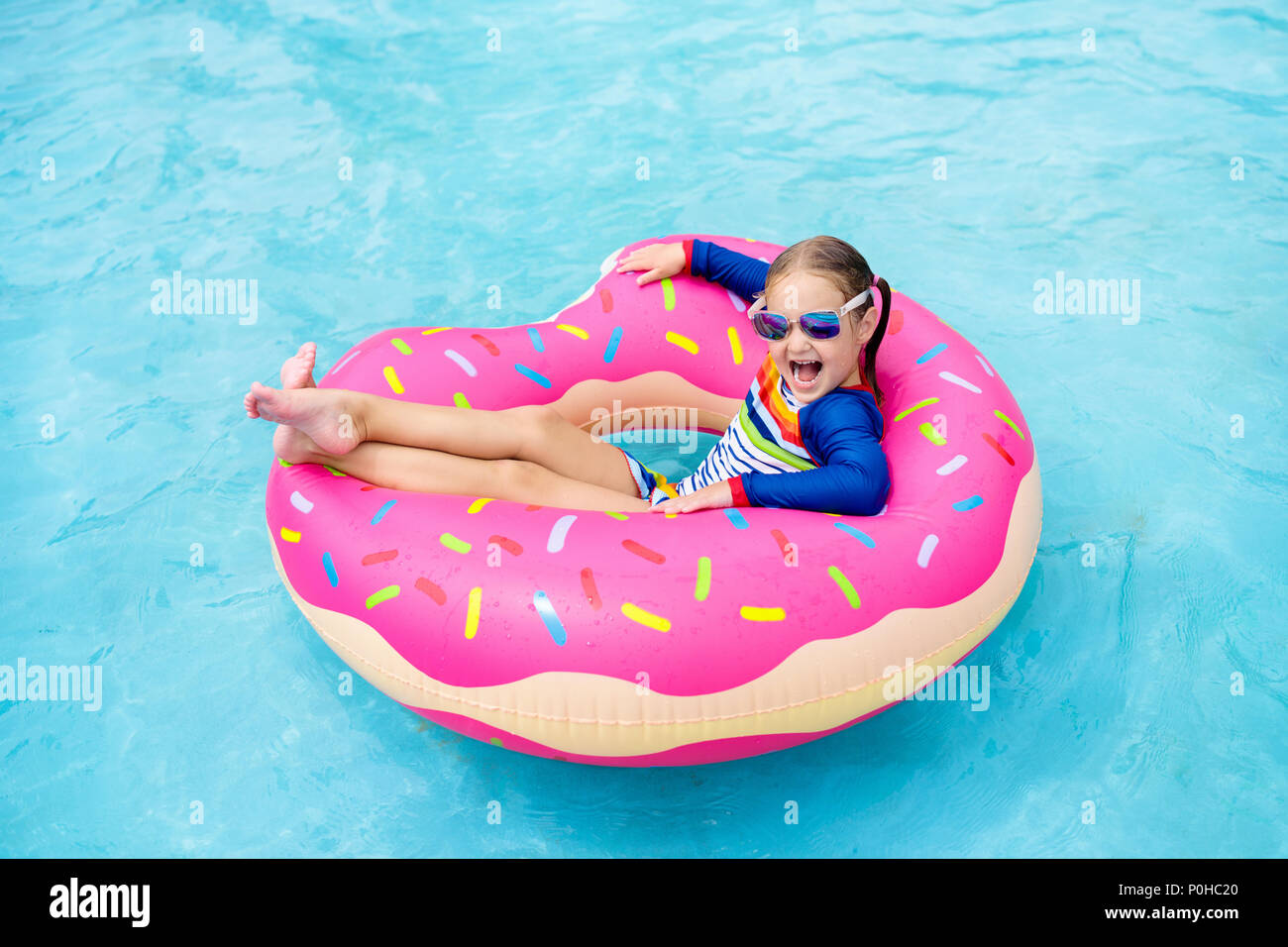 Child in swimming pool on funny inflatable donut float ring. Little