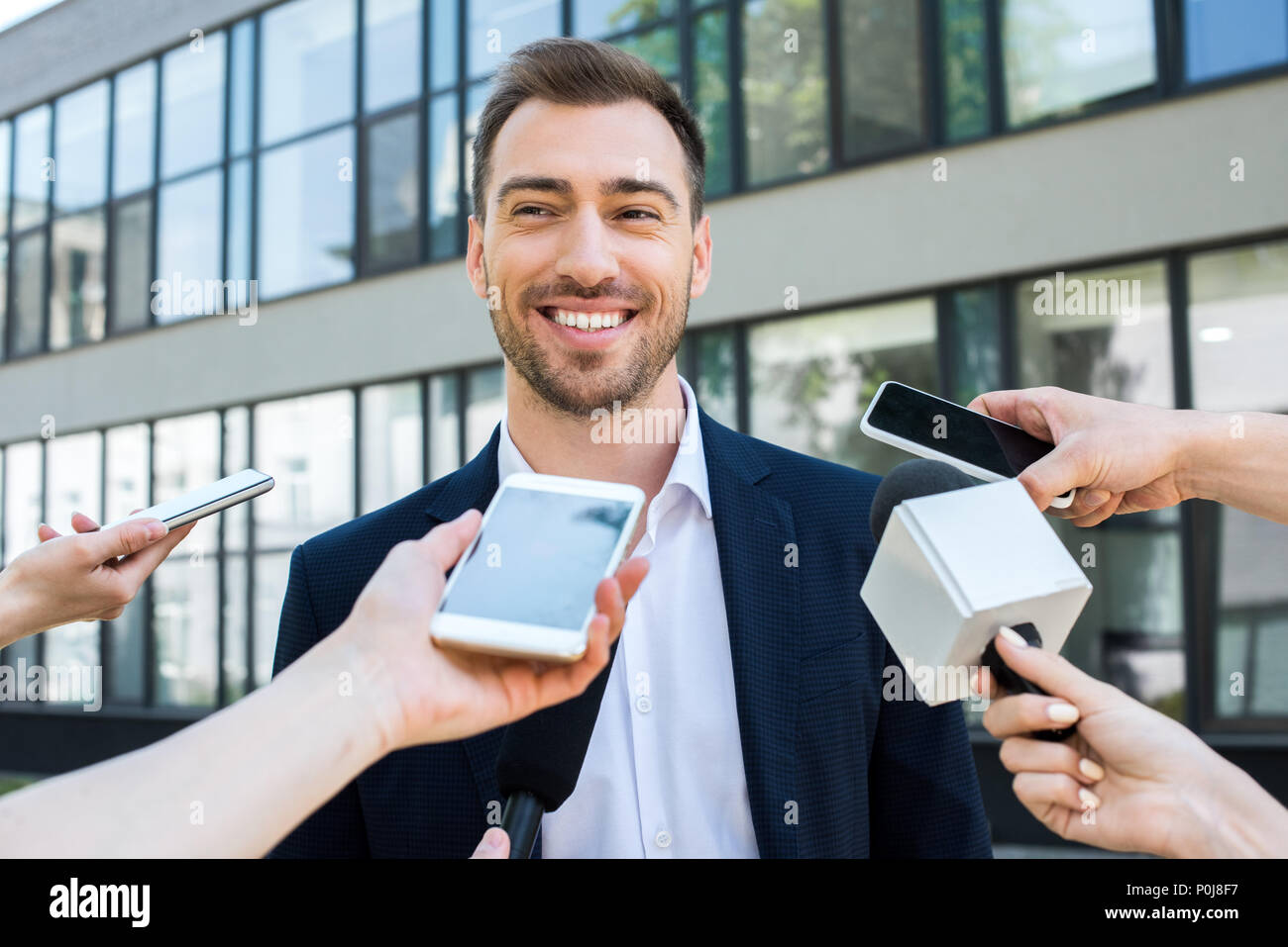 journalists interviewing smiling successful businessman with microphones and smartphones Stock Photo