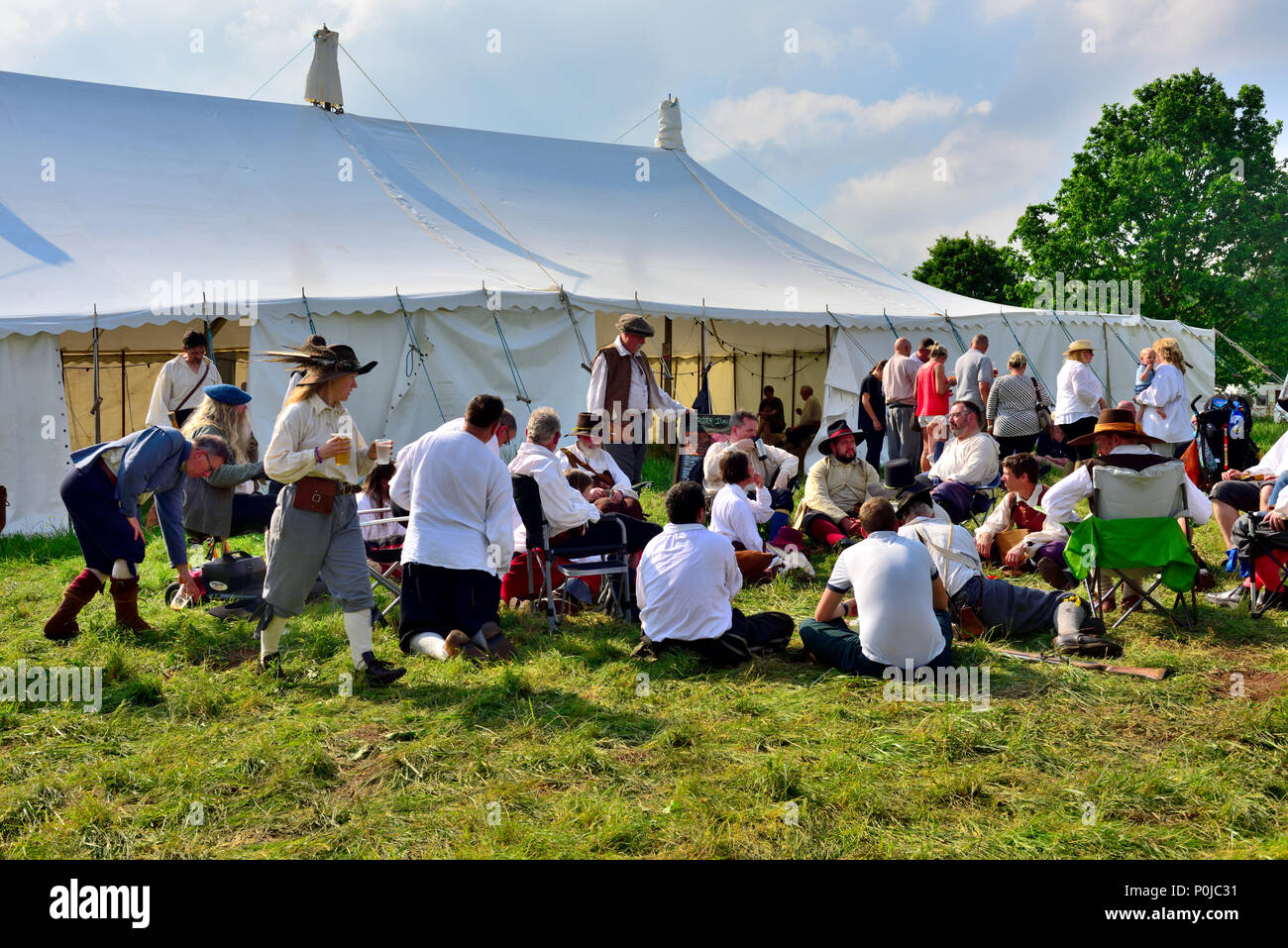 Participants relaxing sitting on grass outside large canvas catering marquee at festival Stock Photo