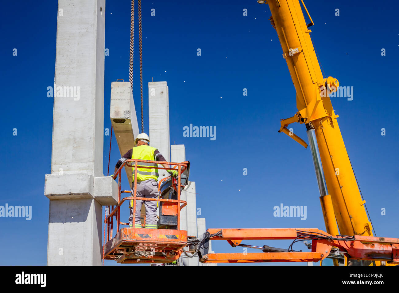 Worker is helping mobile crane to manage concrete joist for assembly ...
