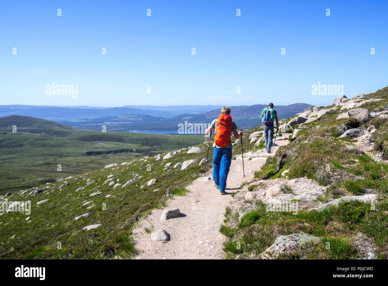 Two hillwalkers / mountaineers with walking poles and backpacks descending mountain path in spring in the Cairngorms National Park, Highland, Scotland Stock Photo
