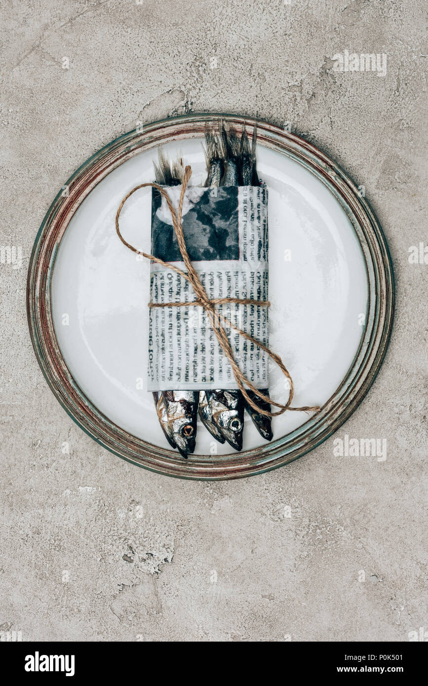 Top view of pile of fish in newspaper wrapped by string on plate Stock