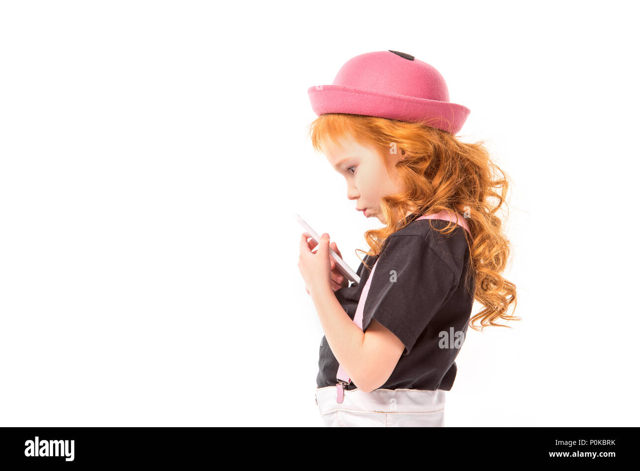 side view of thoughtful red hair kid looking at smartphone isolated on ...