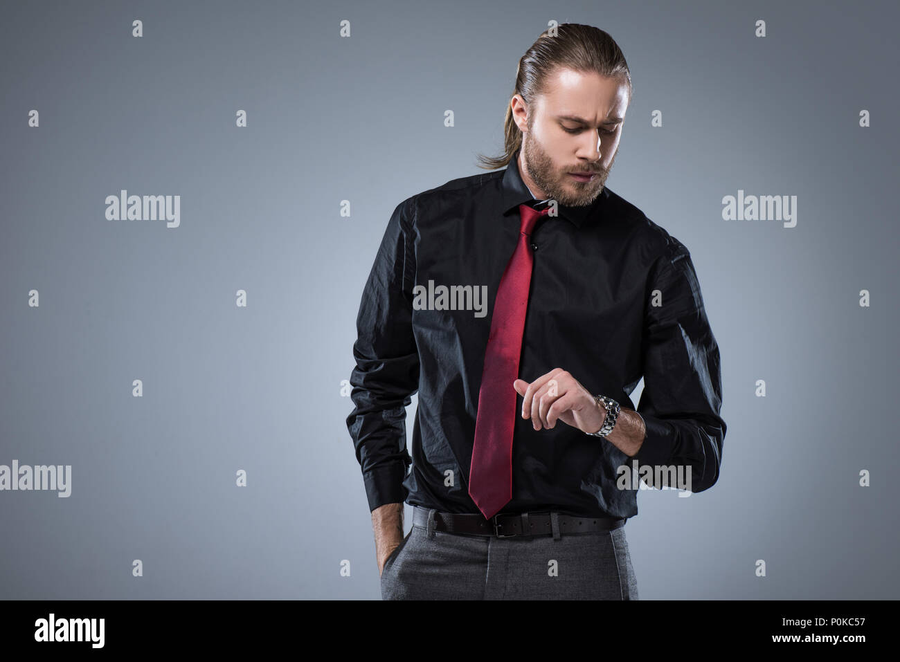 Serious man in black shirt with red tie looking on wristwatch