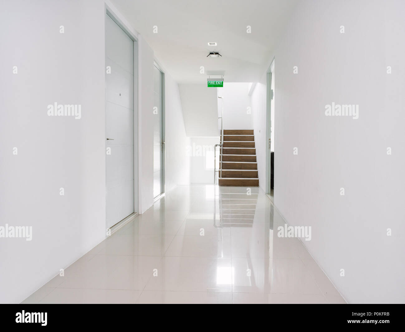 White corridor of the modern building with the exit sign in green and the stair at the end of walkway Stock Photo