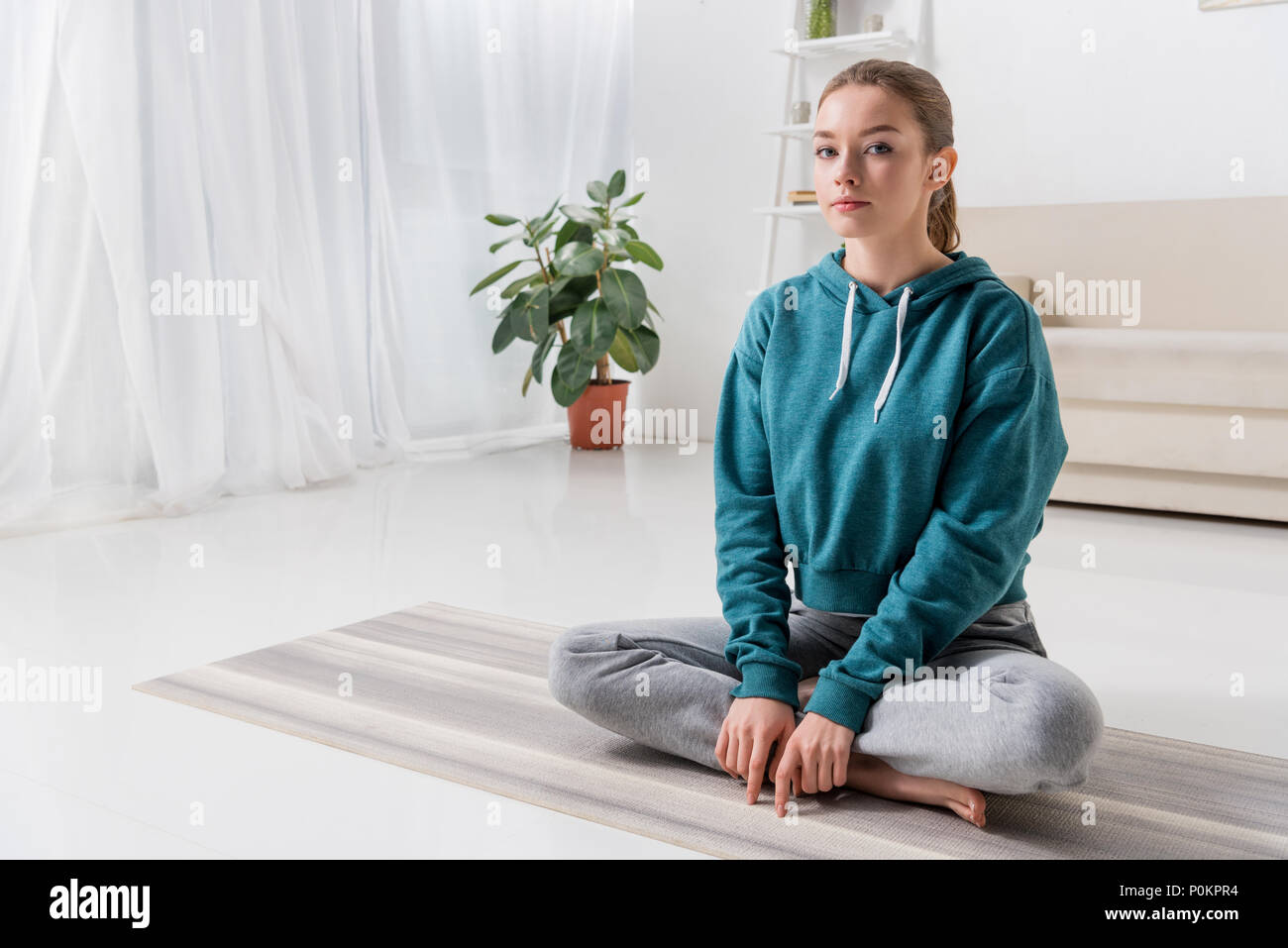 girl sitting in lotus position on yoga mat and looking at camera at ...