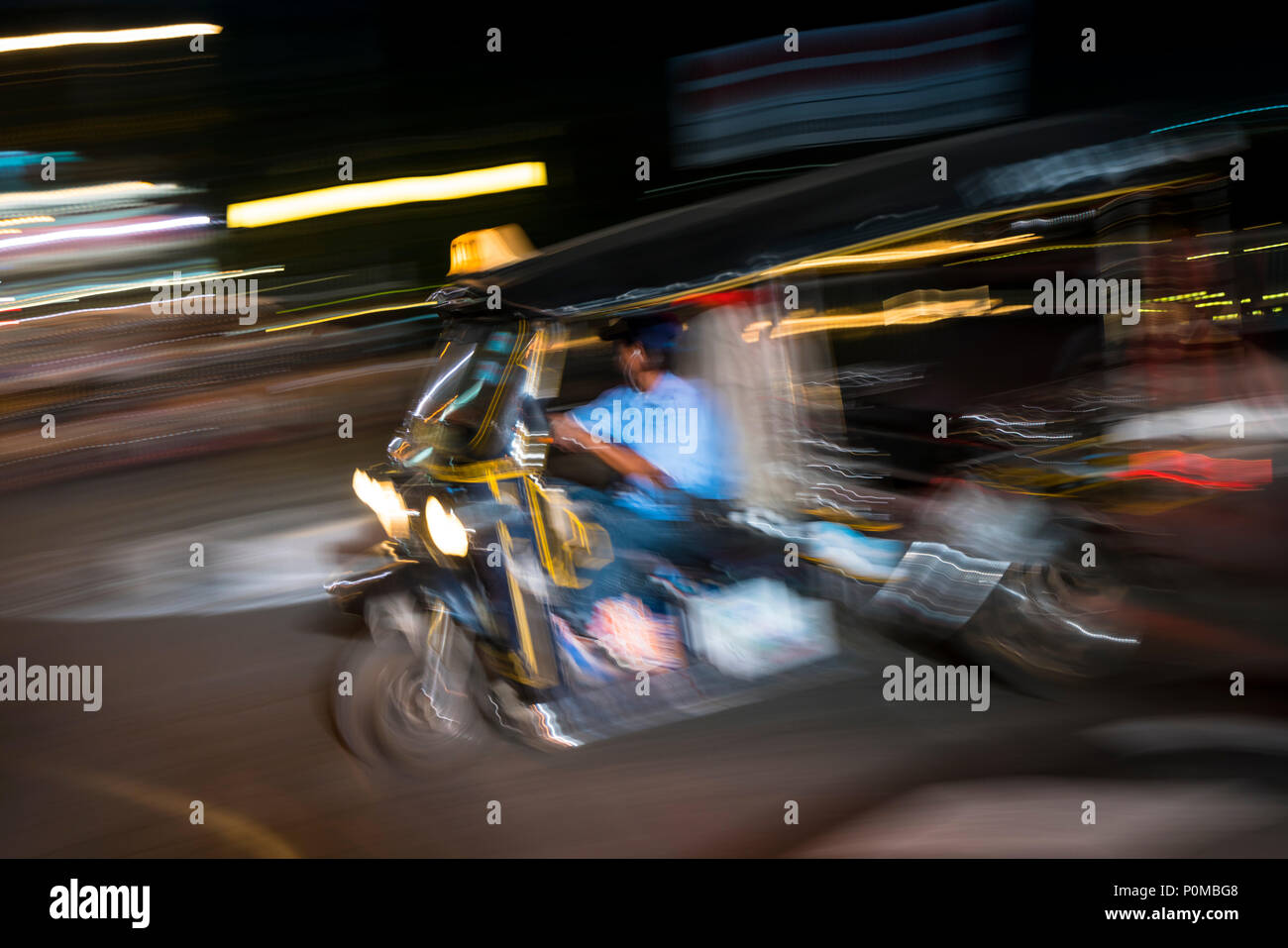 Abstract panning technique creating movement & blur of a tuk-tuk taxi driving at night in the streets of Chiang Mai in northern Thailand Stock Photo