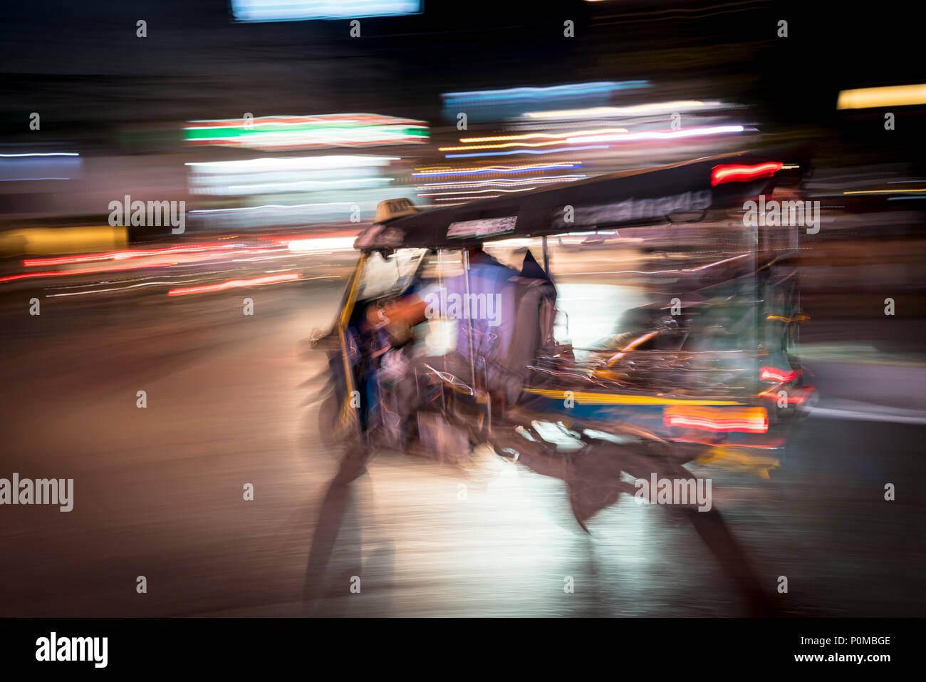 Abstract panning technique creating movement & blur of a tuktuk vehicle driving at night in the streets of Chiang Mai in northern Thailand Stock Photo
