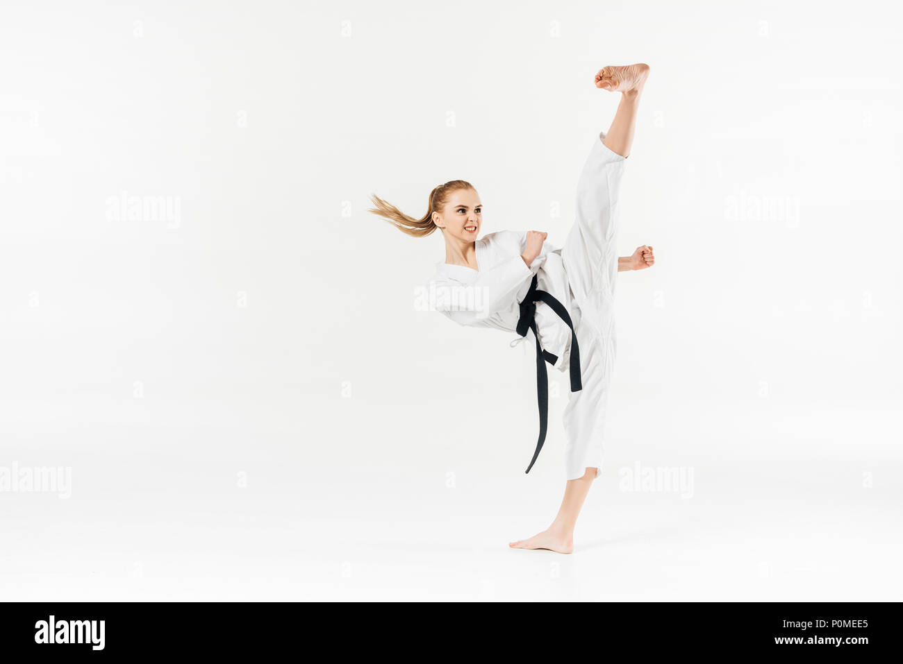 female karate fighter with black belt performing kick isolated on white Stock Photo