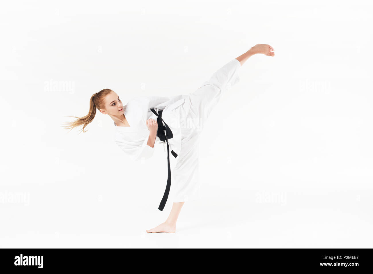 female karate fighter with black belt performing kick isolated on white Stock Photo