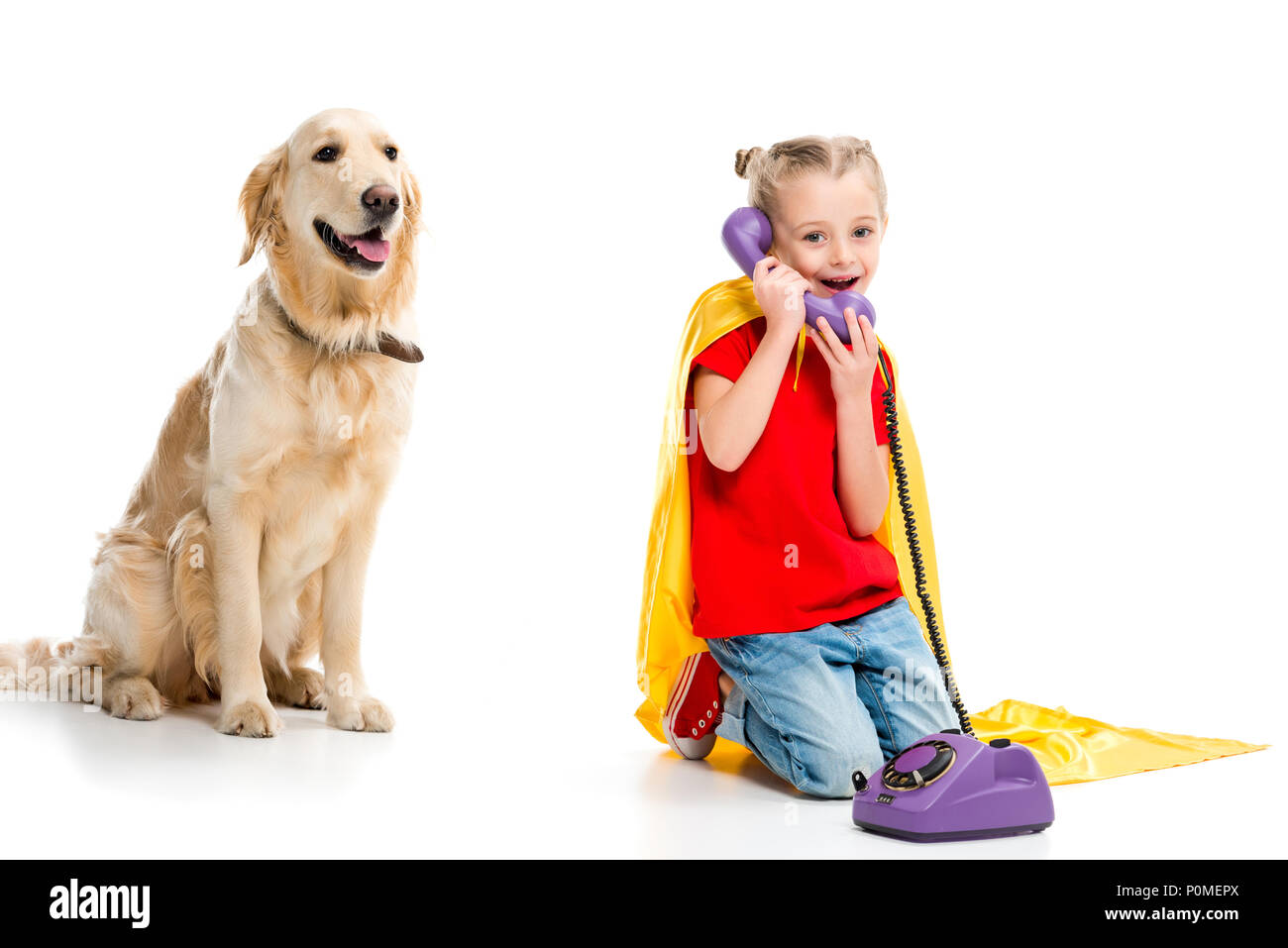 Beige dog with smiling little supergirl talking on phone and wearing yellow cape isolated on white Stock Photo