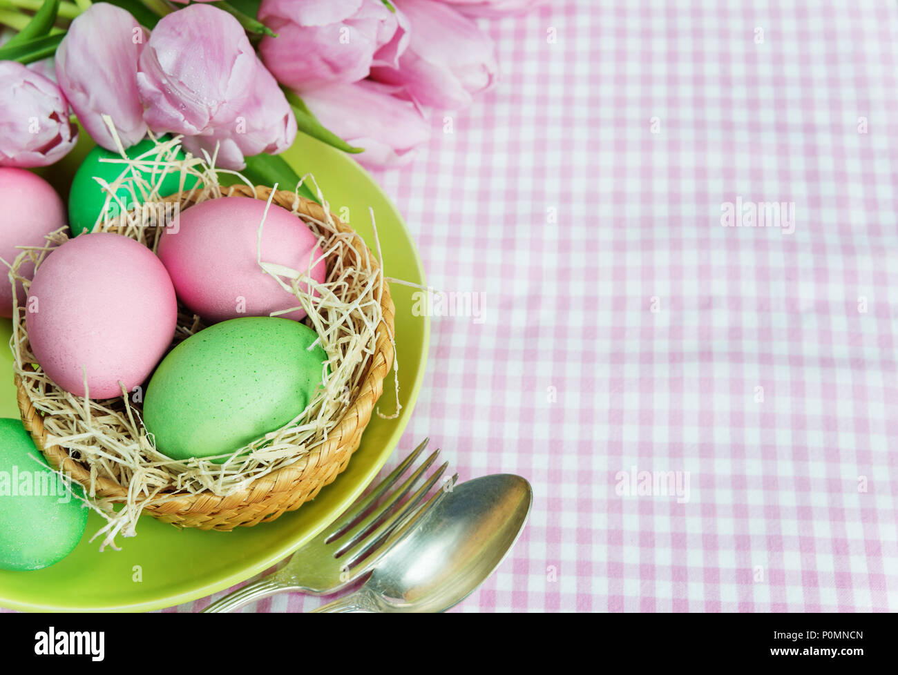 Easter concert: bouquet of pink tulips flowers and Easter eggs, plate and cutlery on checkered tablecloth, with copy-space Stock Photo