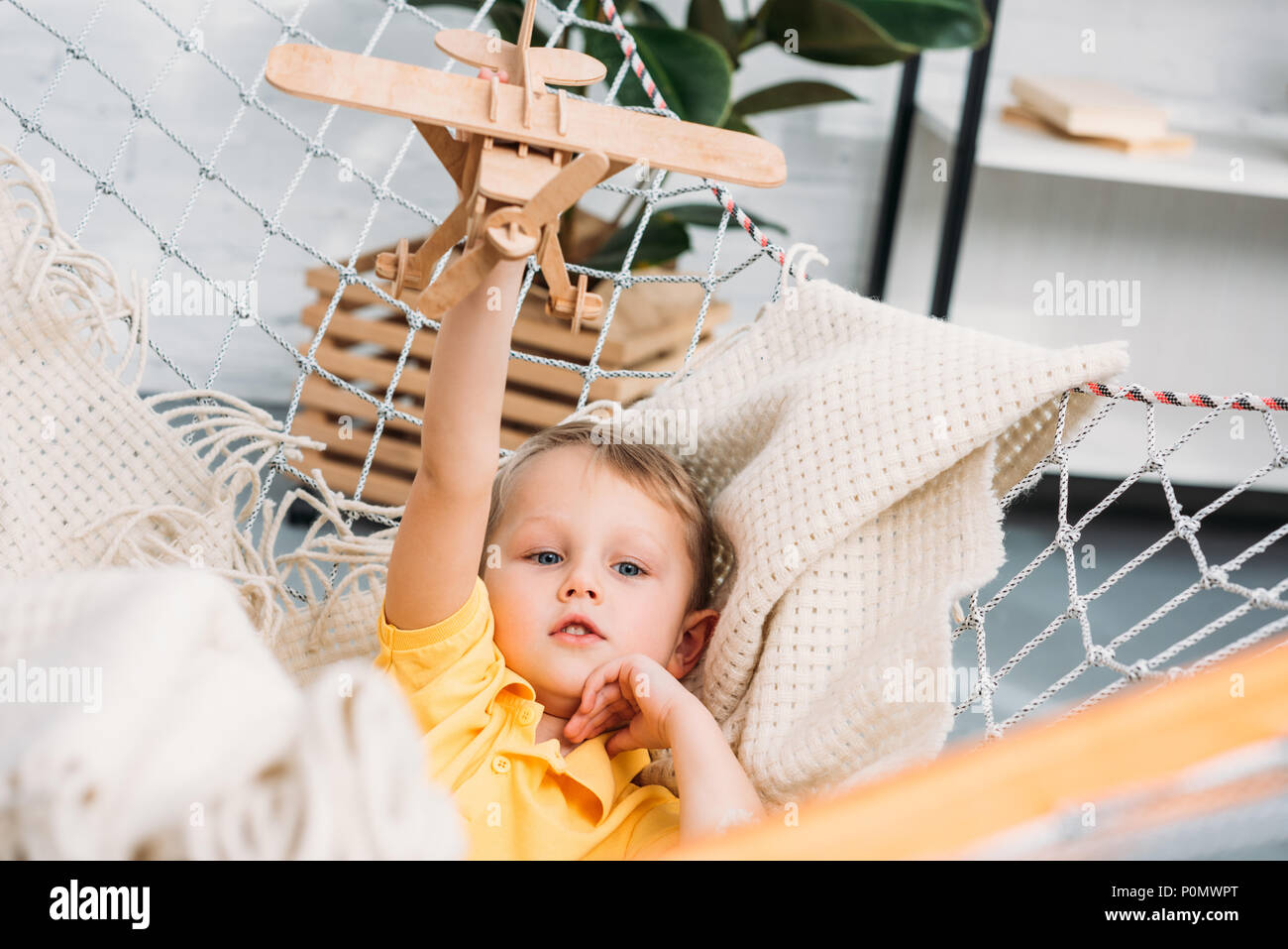 Happy boy playing with wooden airplane toy in hammock Stock Photo