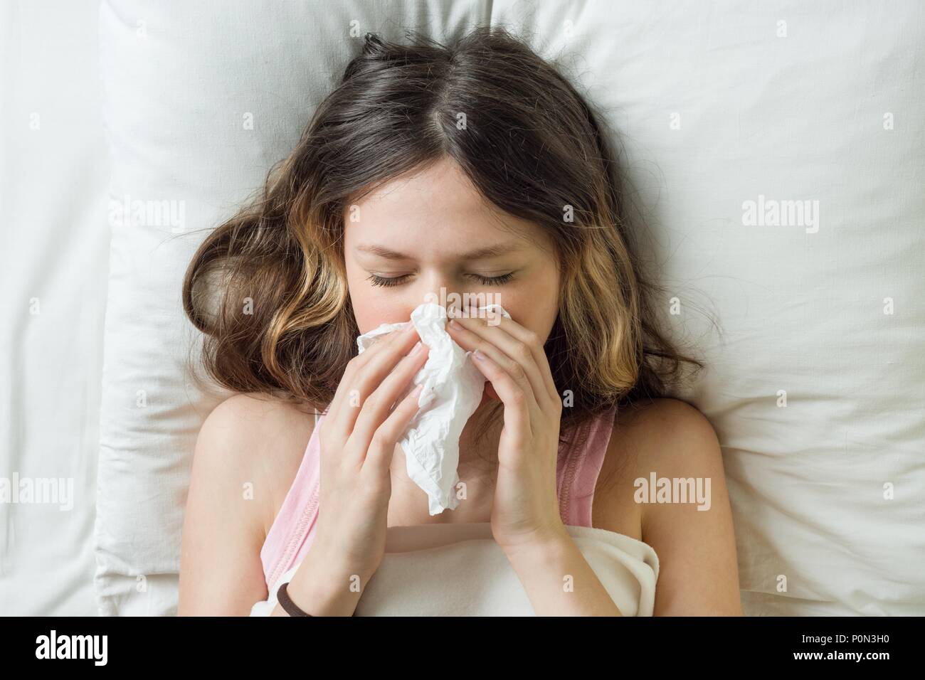 Cold flu season, runny nose. Sick girl on bed sneezing in handkerchief