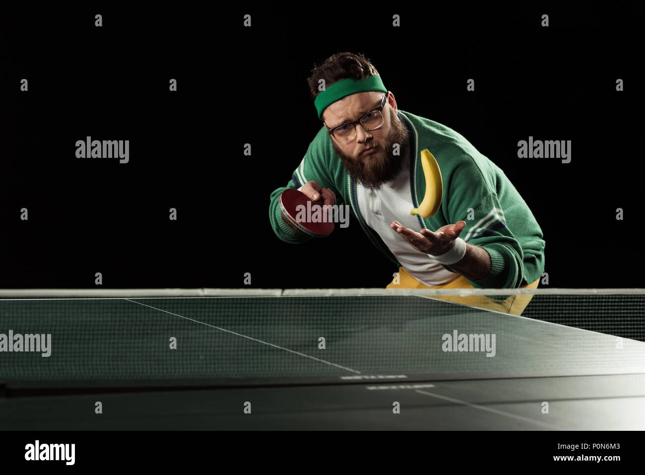 tennis player throwing up banana at tennis table isolated on black